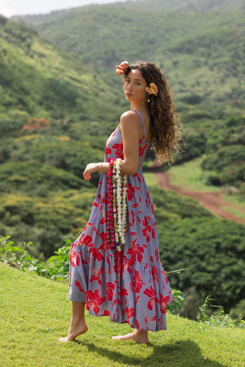 woman with brown hair wearing a flowy maxi dress with periwinkle background and bright red hibiscus print.
