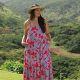 woman with brown hair wearing a flowy maxi dress with periwinkle background and bright red hibiscus print.