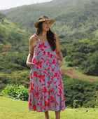 woman with brown hair wearing a flowy maxi dress with periwinkle background and bright red hibiscus print.