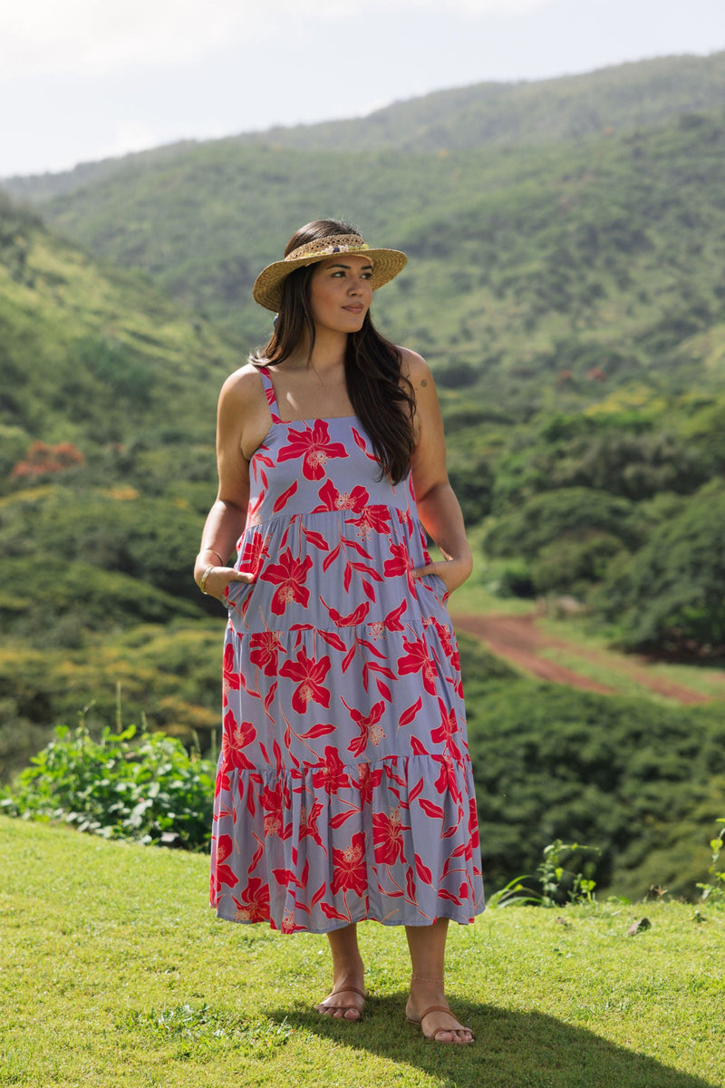 woman with brown hair wearing a flowy maxi dress with periwinkle background and bright red hibiscus print.