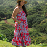 woman with brown hair wearing a flowy maxi dress with periwinkle background and bright red hibiscus print.