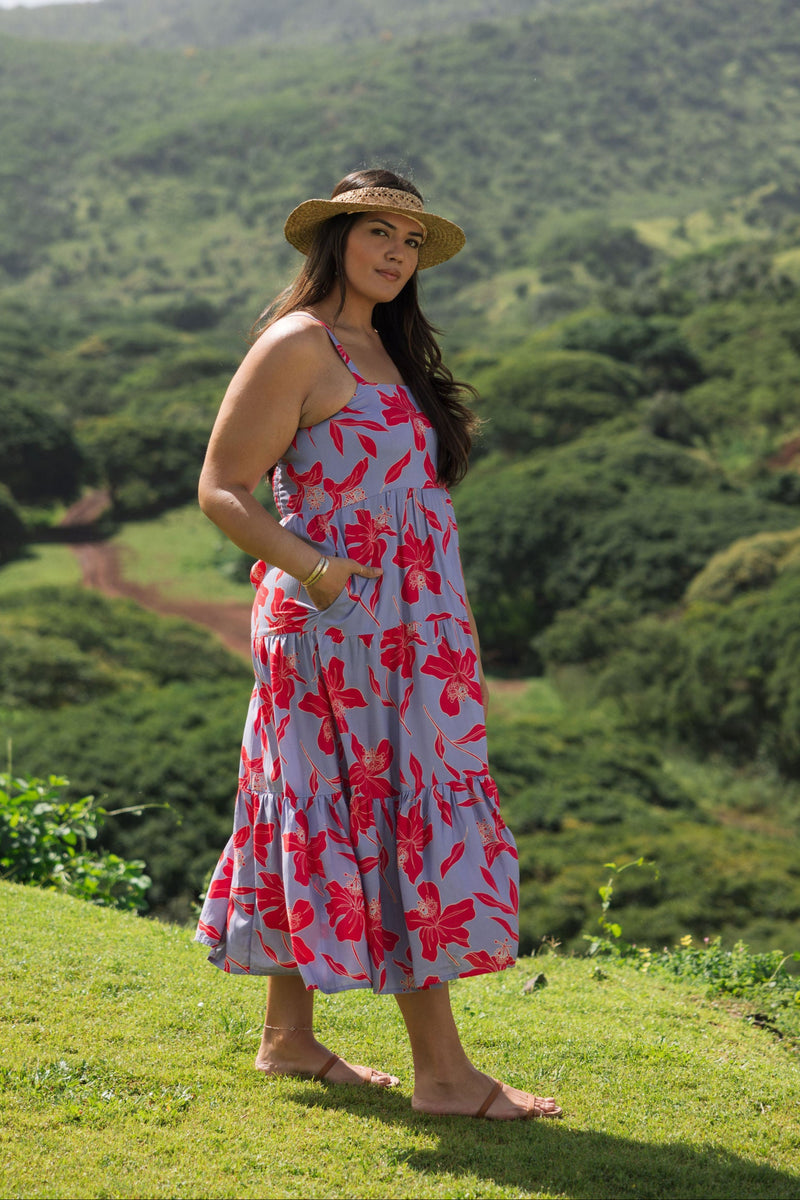woman with brown hair wearing a flowy maxi dress with periwinkle background and bright red hibiscus print.