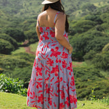 woman with brown hair wearing a flowy maxi dress with periwinkle background and bright red hibiscus print.