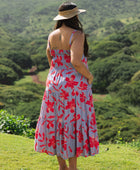 woman with brown hair wearing a flowy maxi dress with periwinkle background and bright red hibiscus print.