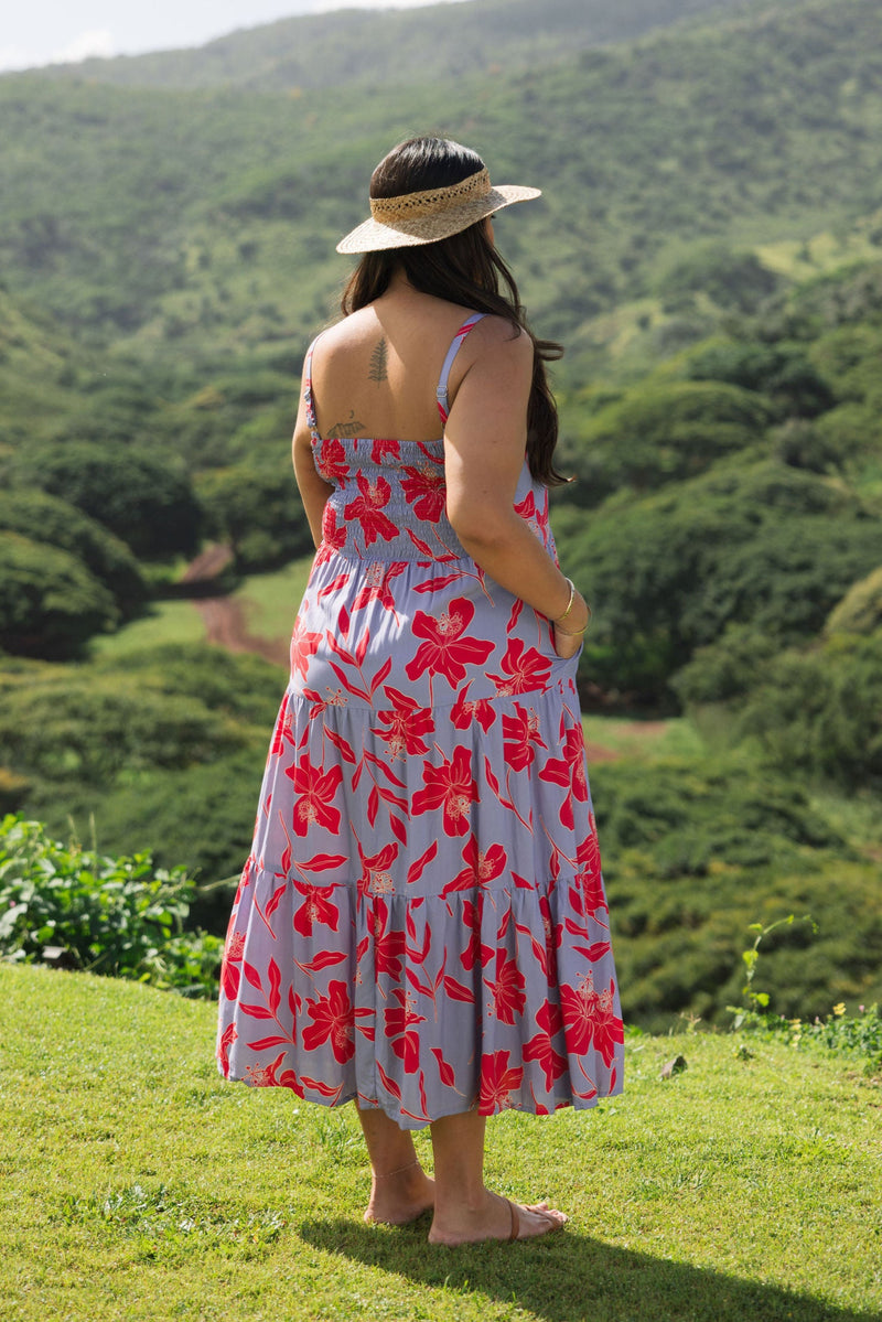 woman with brown hair wearing a flowy maxi dress with periwinkle background and bright red hibiscus print.