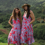 woman with brown hair wearing a flowy maxi dress with periwinkle background and bright red hibiscus print.