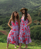 woman with brown hair wearing a flowy maxi dress with periwinkle background and bright red hibiscus print.