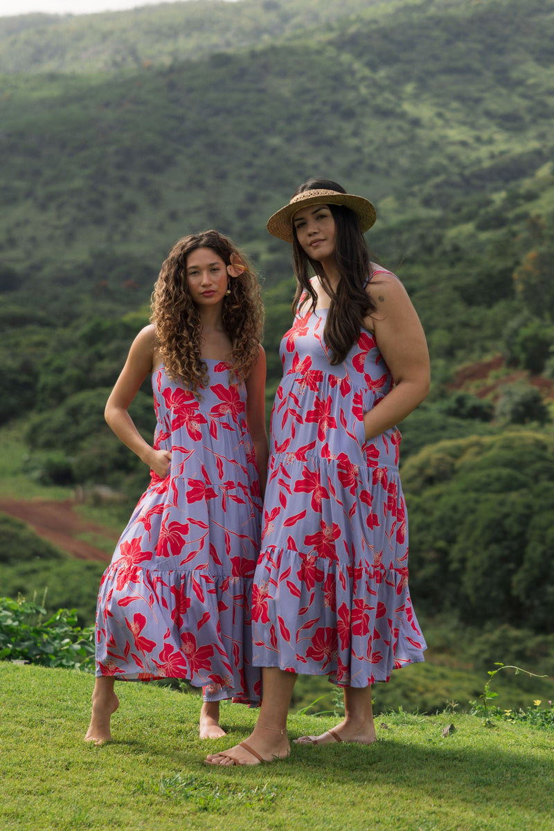 woman with brown hair wearing a flowy maxi dress with periwinkle background and bright red hibiscus print.