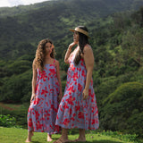 woman with brown hair wearing a flowy maxi dress with periwinkle background and bright red hibiscus print.