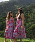woman with brown hair wearing a flowy maxi dress with periwinkle background and bright red hibiscus print.