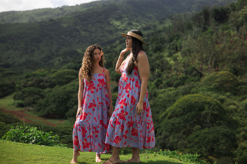 woman with brown hair wearing a flowy maxi dress with periwinkle background and bright red hibiscus print.