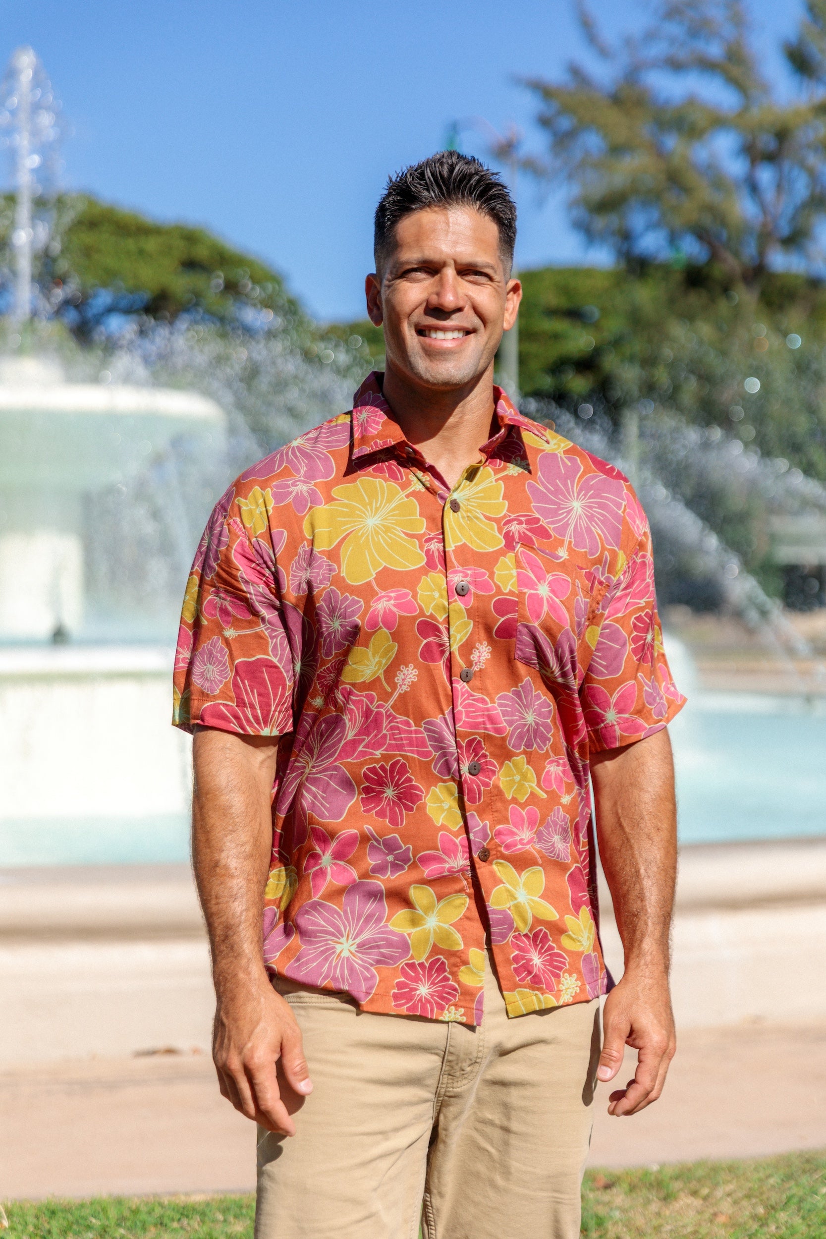 man wearing terracotta colored aloha shirt with large purple and yellow flower print