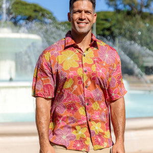 man wearing terracotta colored aloha shirt with large purple and yellow flower print