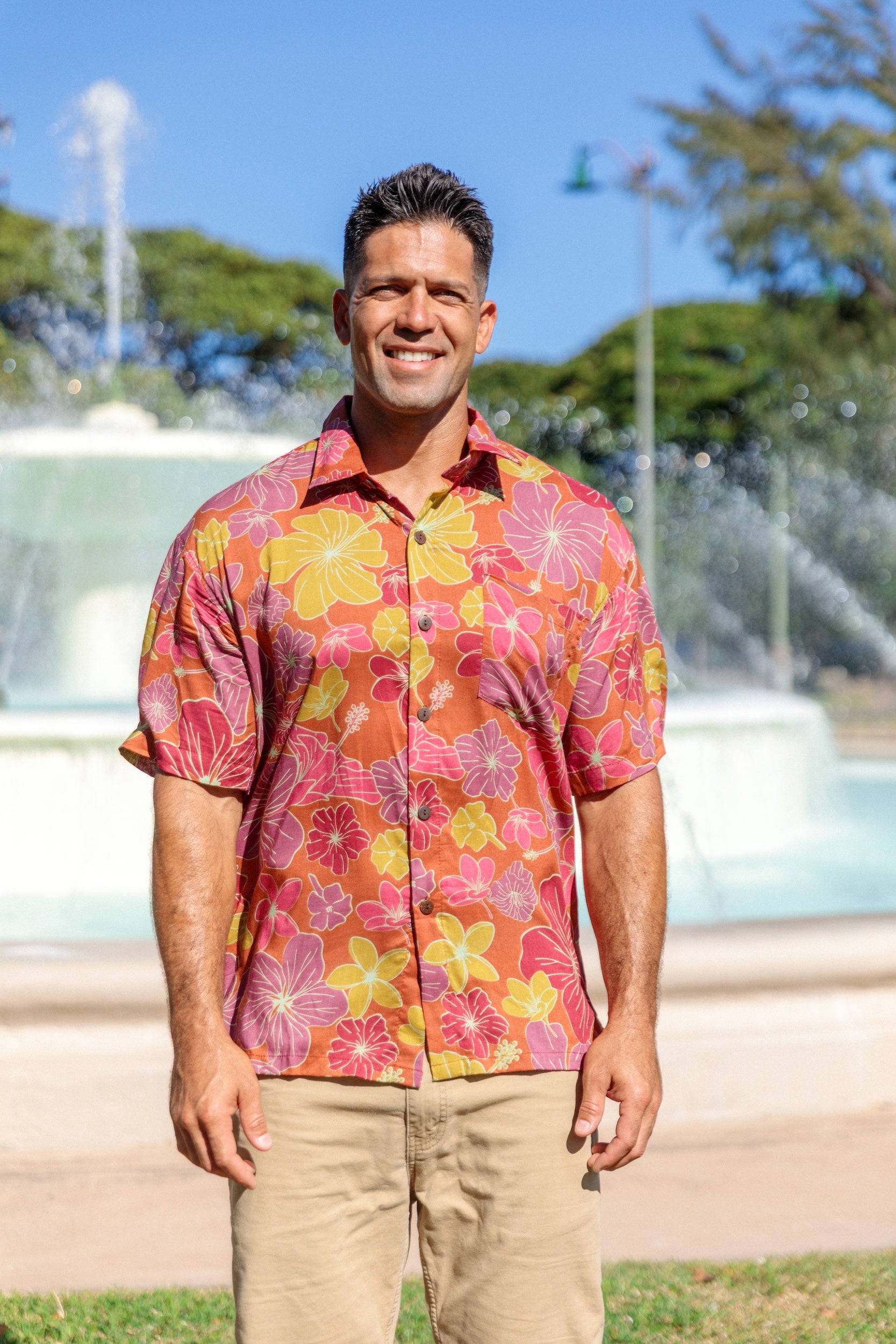man wearing terracotta colored aloha shirt with large purple and yellow flower print