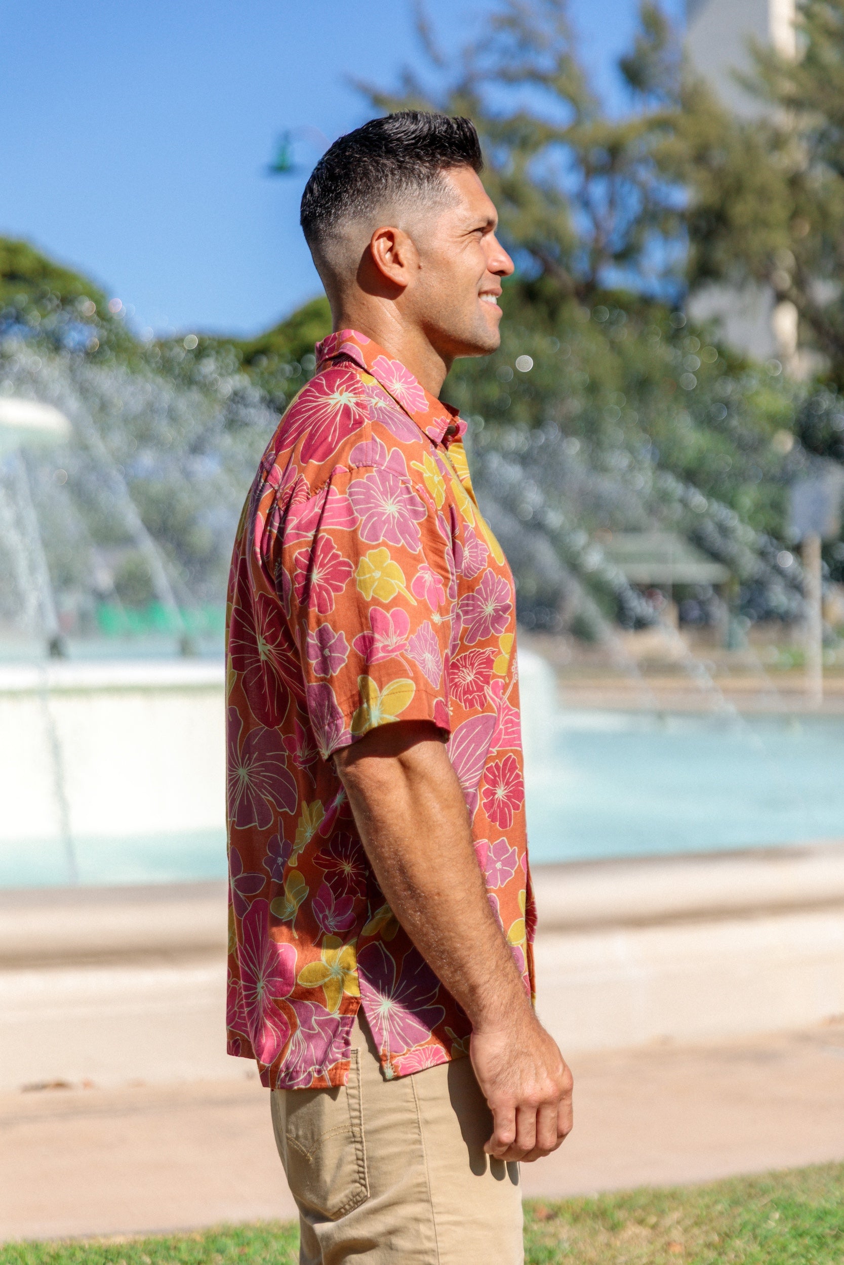man wearing terracotta colored aloha shirt with large purple and yellow flower print