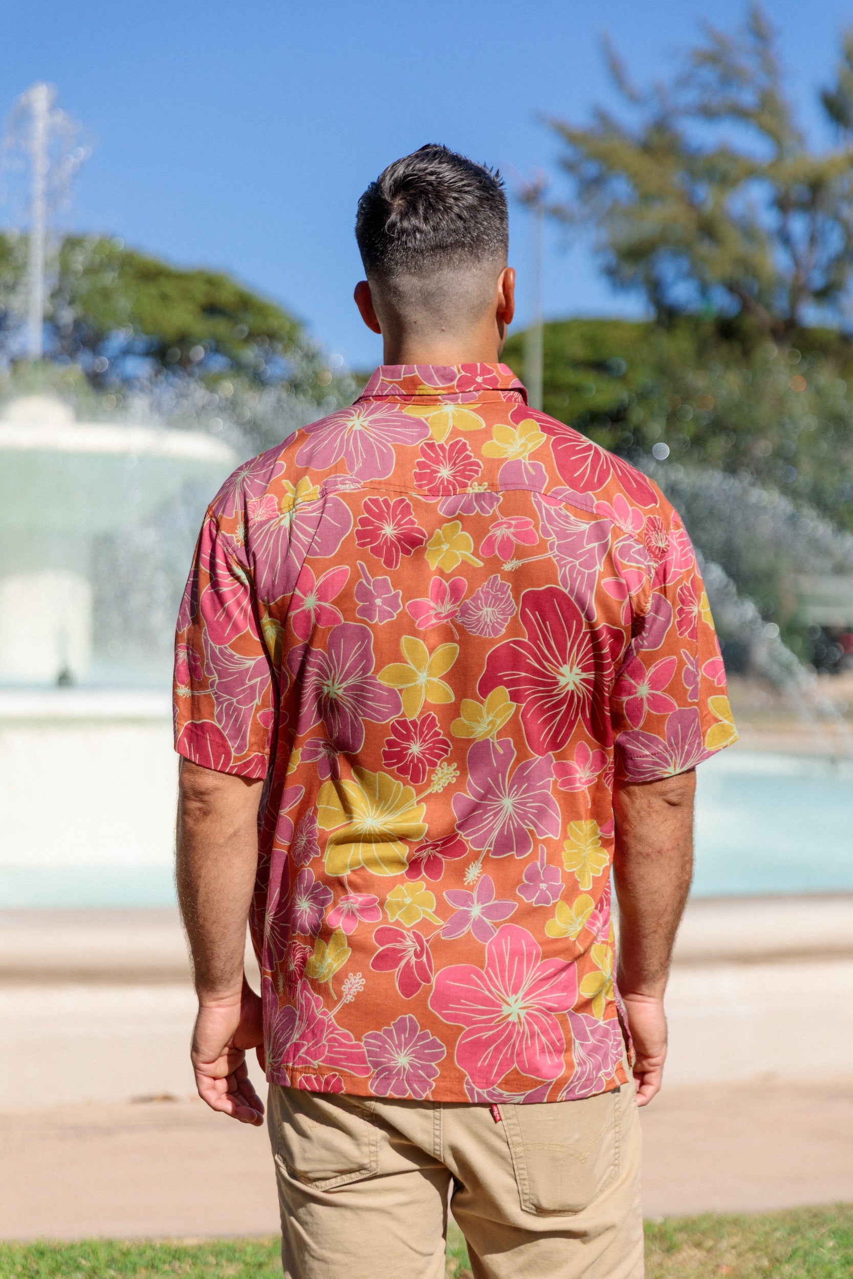 man wearing terracotta colored aloha shirt with large purple and yellow flower print