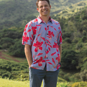 man with brown hair wearing a button up aloha shirt with periwinkle background and bright red hibiscus print.