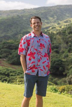 man with brown hair wearing a button up aloha shirt with periwinkle background and bright red hibiscus print.