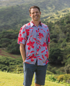 man with brown hair wearing a button up aloha shirt with periwinkle background and bright red hibiscus print.