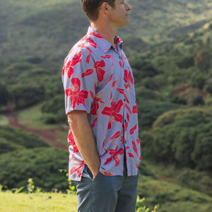 man with brown hair wearing a button up aloha shirt with periwinkle background and bright red hibiscus print.