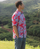 man with brown hair wearing a button up aloha shirt with periwinkle background and bright red hibiscus print.