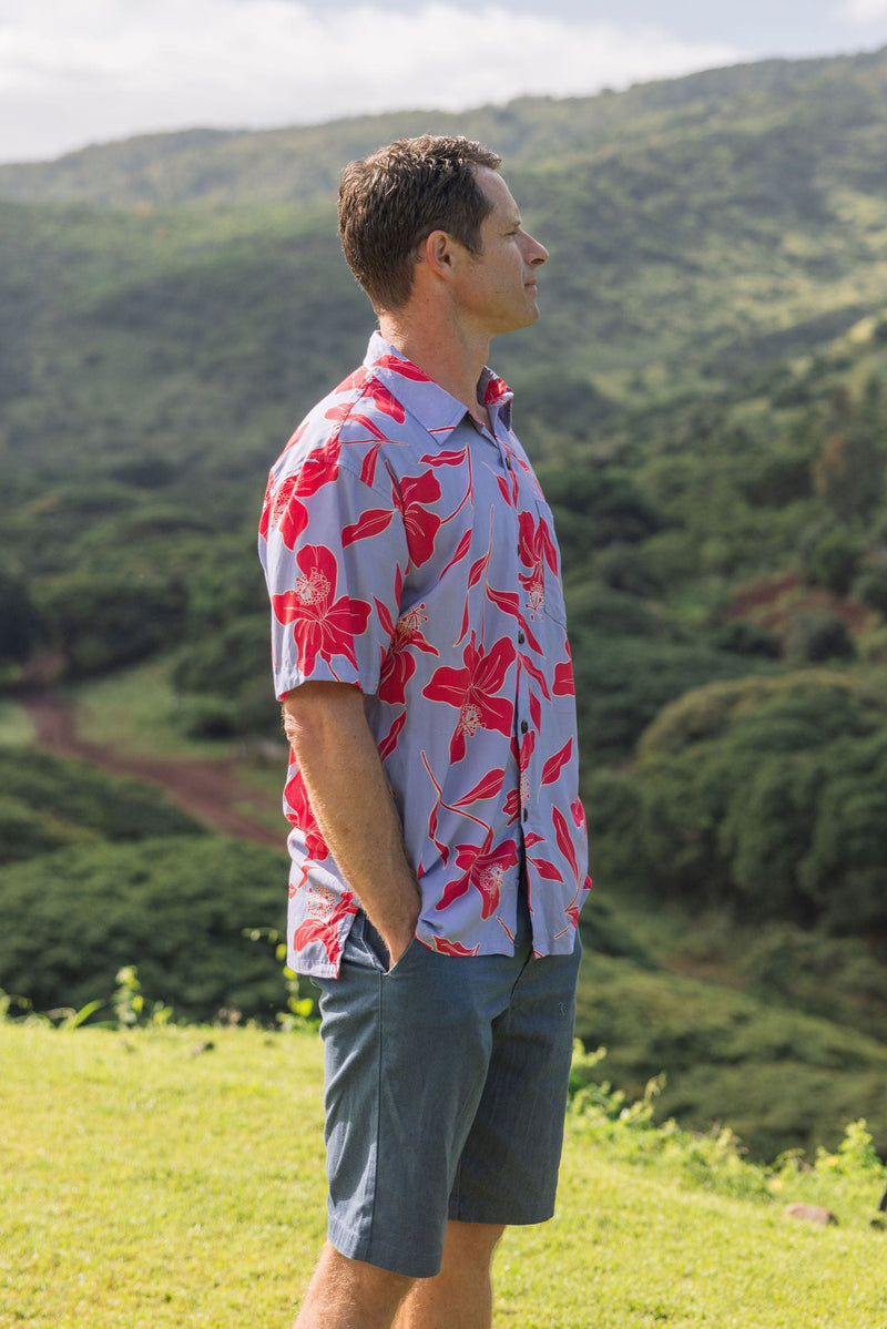 man with brown hair wearing a button up aloha shirt with periwinkle background and bright red hibiscus print.