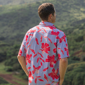 man with brown hair wearing a button up aloha shirt with periwinkle background and bright red hibiscus print.
