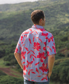 man with brown hair wearing a button up aloha shirt with periwinkle background and bright red hibiscus print.