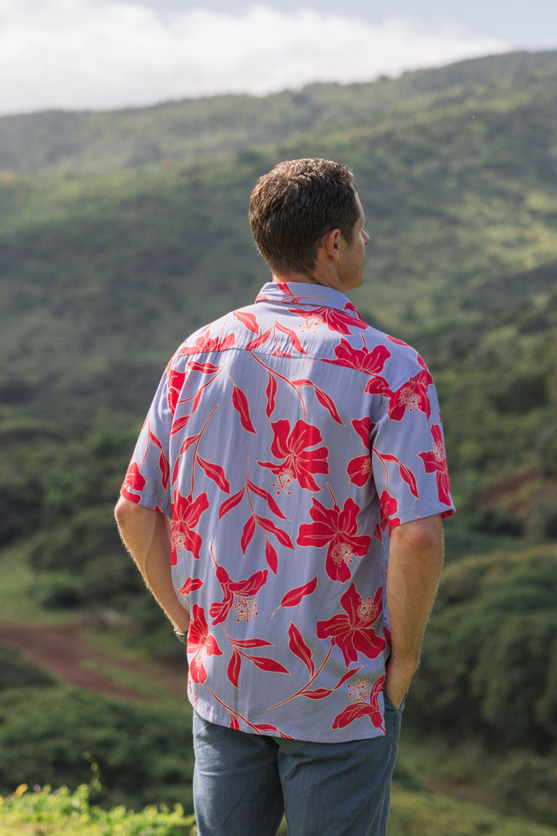 man with brown hair wearing a button up aloha shirt with periwinkle background and bright red hibiscus print.