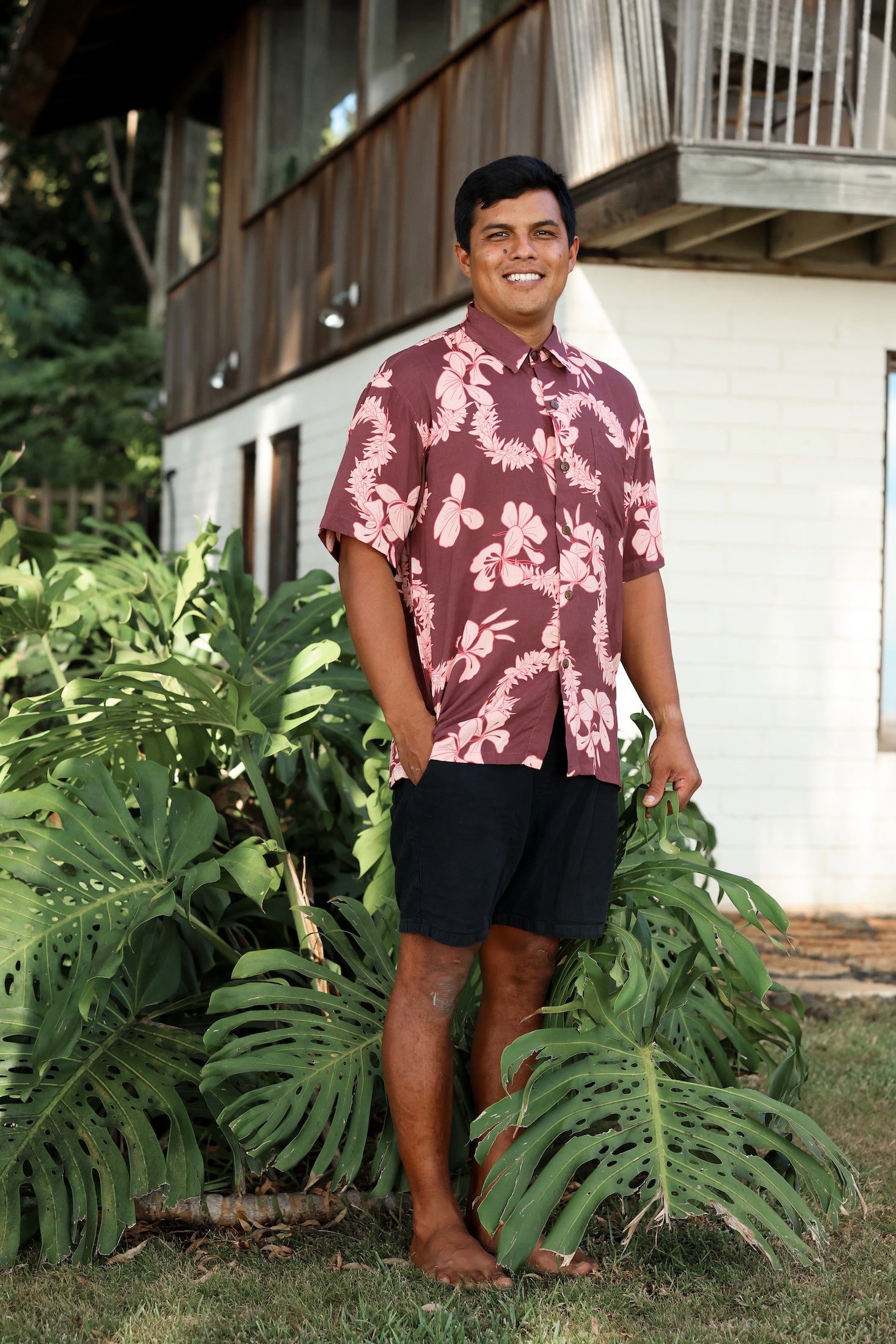man wearing brown aloha shirt with pink lei awapuhi print