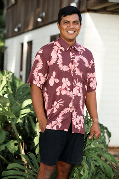 man wearing brown aloha shirt with pink lei awapuhi print