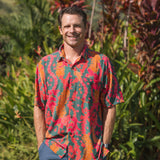 man with brown hair wearing a colorful button up aloha shirt with tropical lei print