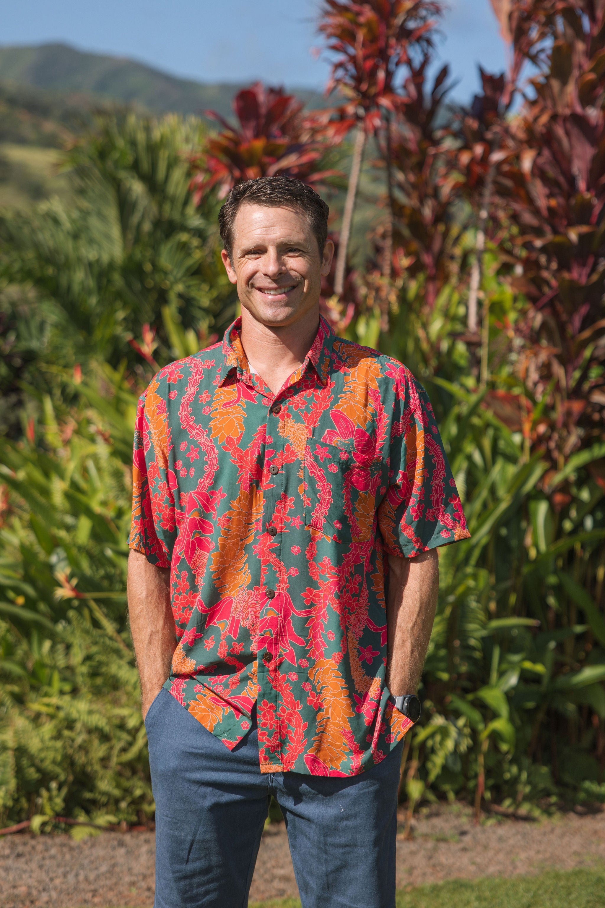 man with brown hair wearing a colorful button up aloha shirt with tropical lei print