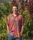 man with brown hair wearing a colorful button up aloha shirt with tropical lei print