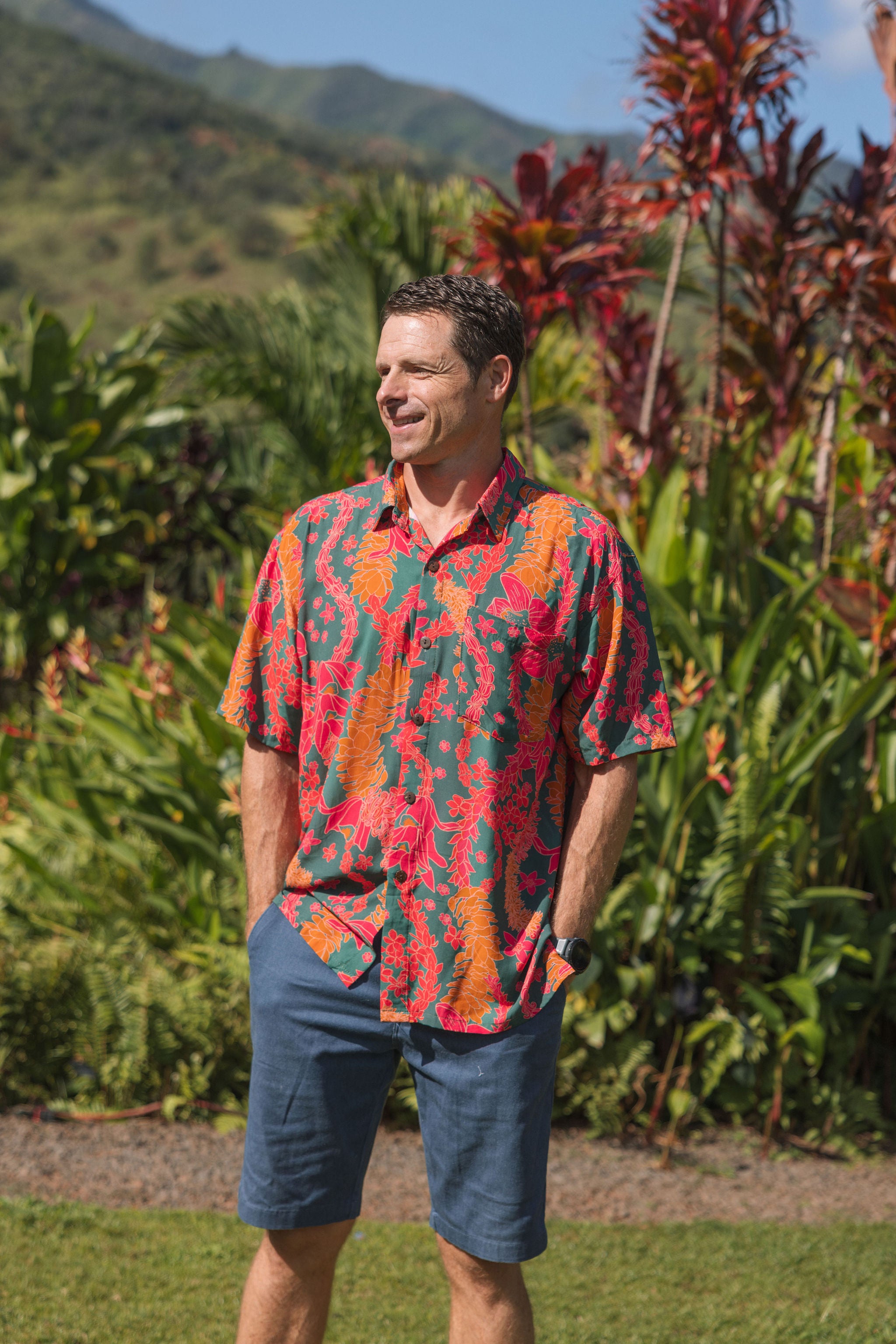 man with brown hair wearing a colorful button up aloha shirt with tropical lei print