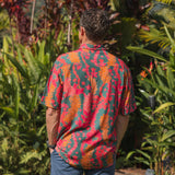 man with brown hair wearing a colorful button up aloha shirt with tropical lei print