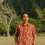 man with black hair wearing a red-brown aloha button up shirt with lei print