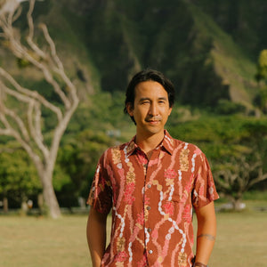 man with black hair wearing a red-brown aloha button up shirt with lei print