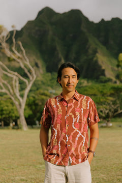 man with black hair wearing a red-brown aloha button up shirt with lei print