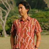 man with black hair wearing a red-brown aloha button up shirt with lei print