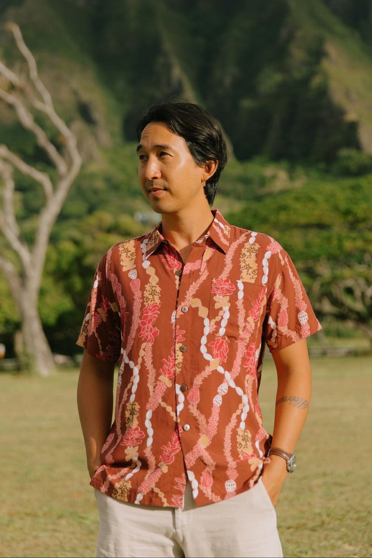 man with black hair wearing a red-brown aloha button up shirt with lei print