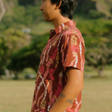 man with black hair wearing a red-brown aloha button up shirt with lei print