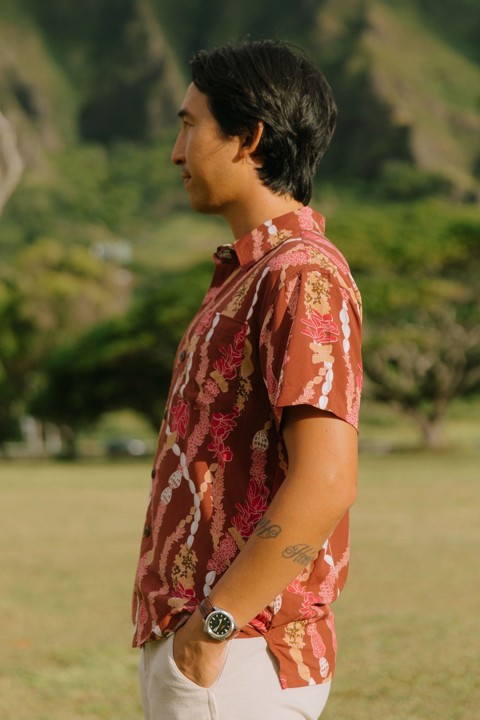 man with black hair wearing a red-brown aloha button up shirt with lei print