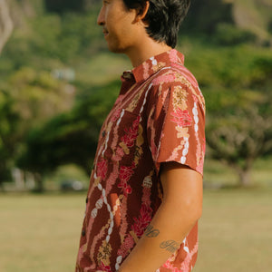 man with black hair wearing a red-brown aloha button up shirt with lei print