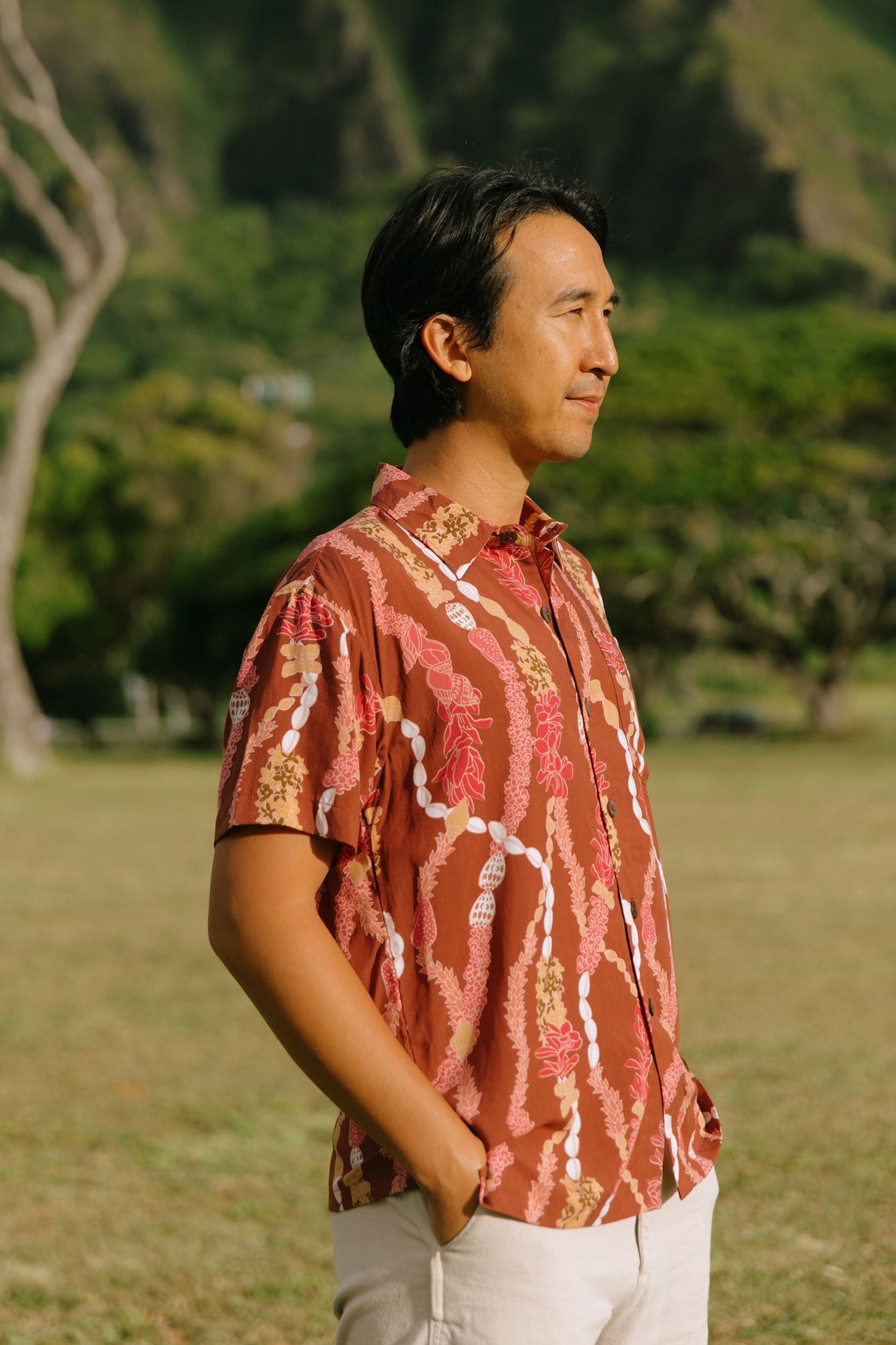 man with black hair wearing a red-brown aloha button up shirt with lei print