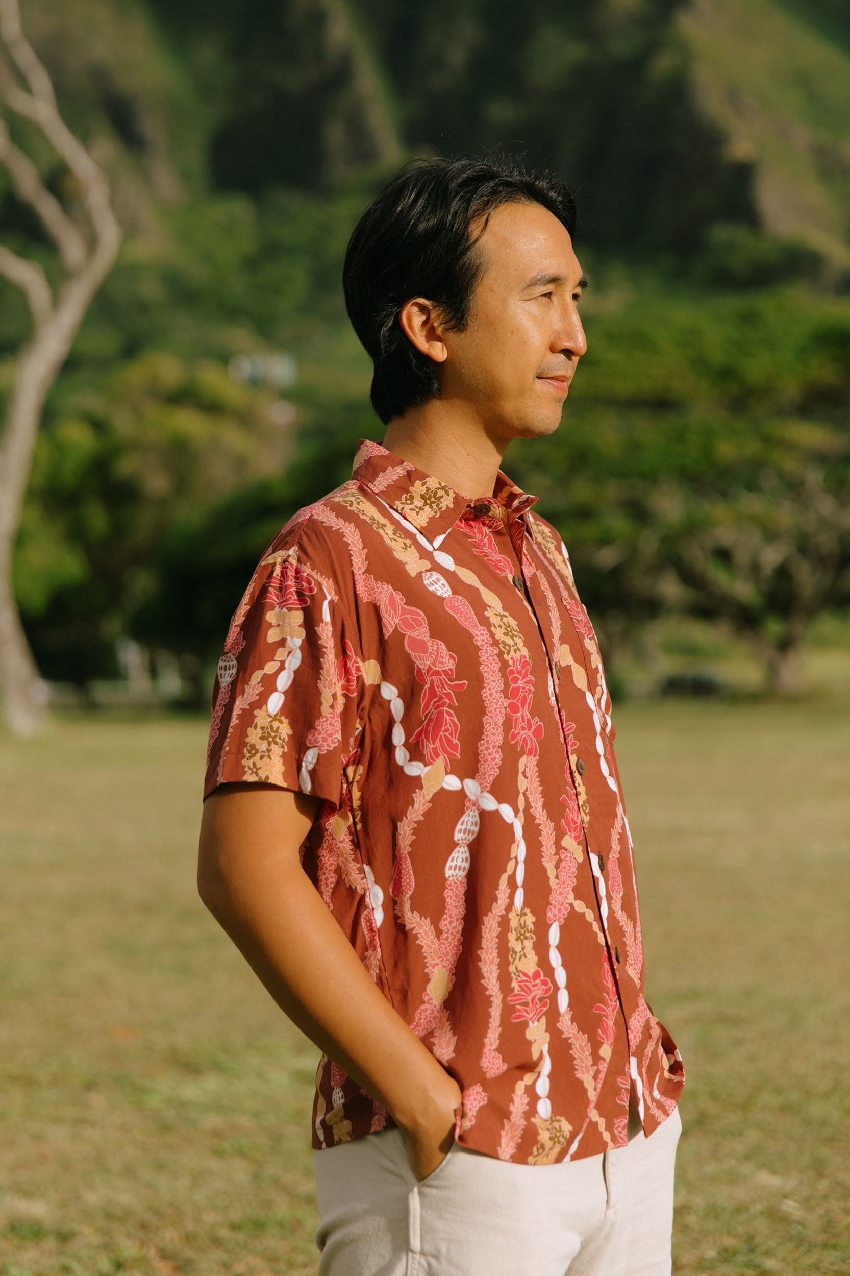 man with black hair wearing a red-brown aloha button up shirt with lei print