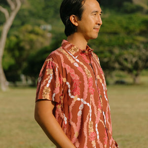 man with black hair wearing a red-brown aloha button up shirt with lei print