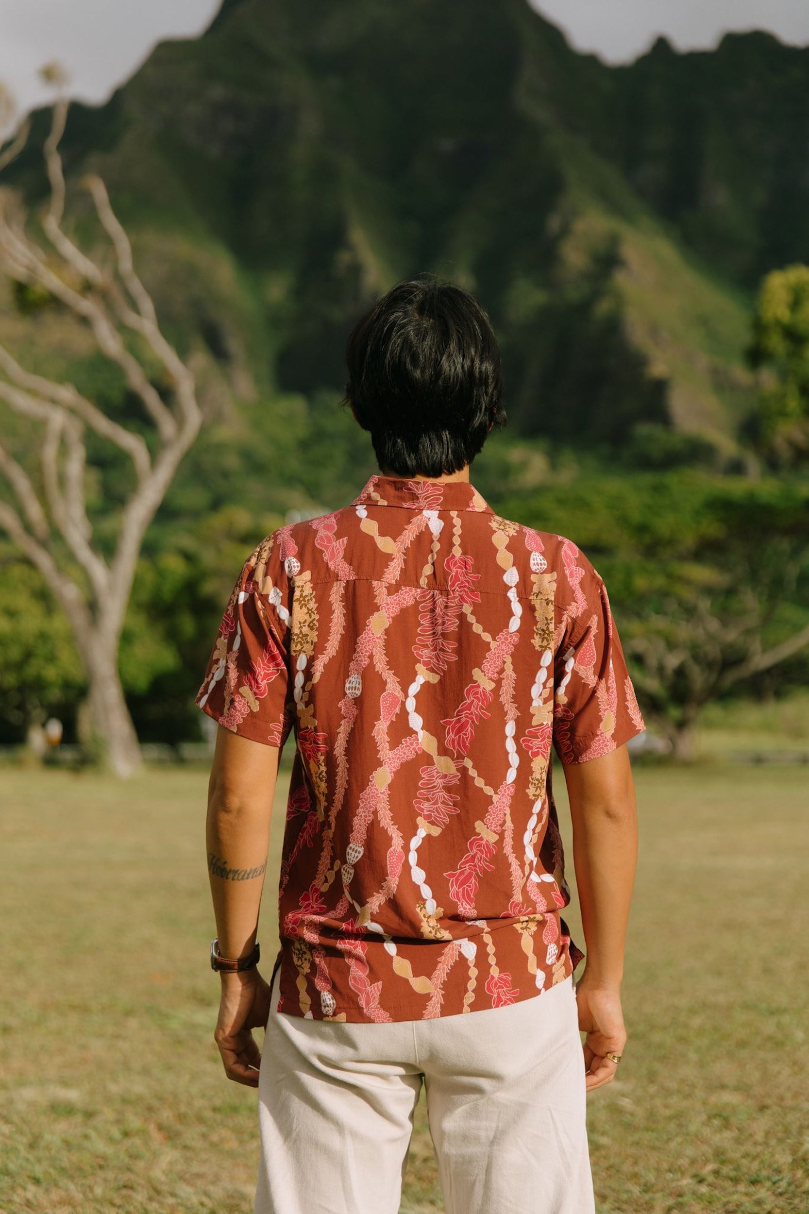 man with black hair wearing a red-brown aloha button up shirt with lei print