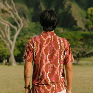 man with black hair wearing a red-brown aloha button up shirt with lei print