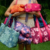 woman holding an expandable neoprene travel pouch with palaka and kokio print